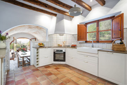Helle Landhausküche mit Holzbalken, Terrakottaboden und Blick ins Esszimmer mit Zugang zur Terrasse
